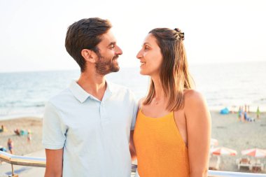 Tatilde mutlu ve kendinden emin gülümseyen genç bir çift. Yüzünde gülümsemeyle sahilde sarılırken
