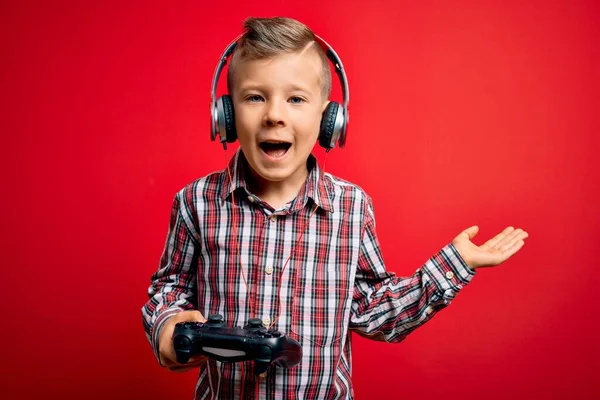 赤の背景にゲームパッドジョイスティックを使用してビデオゲームをプレイ若い小さな白人ゲーマーの子供は非常に幸せと興奮し 大きな笑顔で叫んで勝利を祝う勝者の式と手を上げ — ストック写真