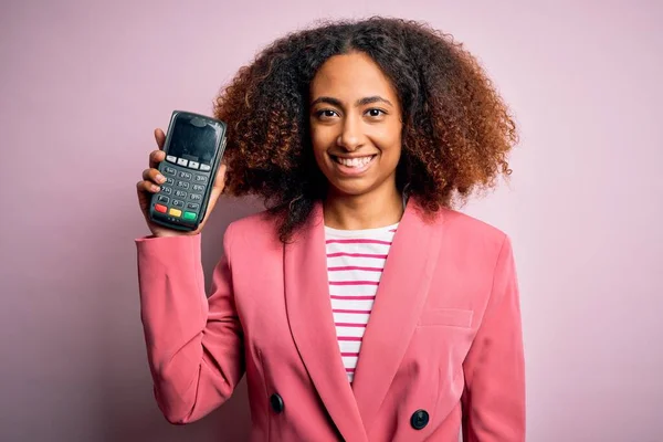 Young african american woman with afro hair holding dataphone over pink background with a happy face standing and smiling with a confident smile showing teeth