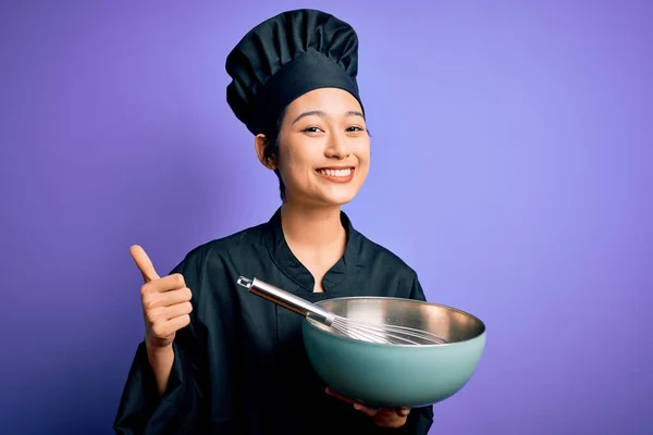 年轻美丽的中国厨师 身穿炊事服 头戴大头帽 头戴碗 带着大大的笑容 高兴地做着好手势 用手指竖起大拇指 是极好的标志 — 图库照片
