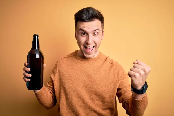 黄色の背景の上にビールのボトルを飲む若いハンサムな白人男性は誇りと勝利と成功を祝う叫んで非常に興奮し 感情を応援 — ストック写真