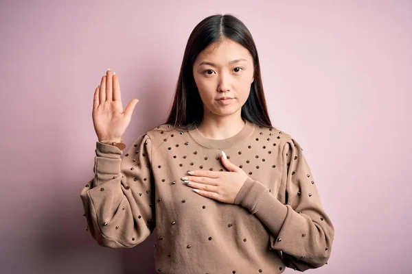 年轻美丽的亚洲女人 穿着时尚和典雅的毛衣 穿着粉色的 舒适的背景 双手放在胸前 张开手掌 宣誓效忠 — 图库照片