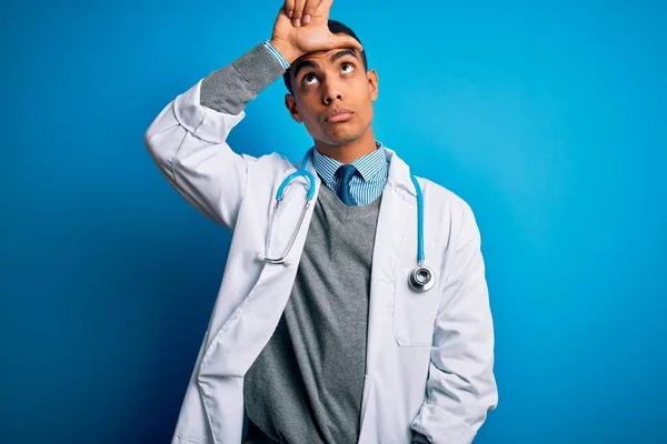 英俊的非洲裔美国医生 身穿外套 带着听诊器的蓝色背景的男人取笑额头上有手指的人做失败者的手势 嘲笑和侮辱 — 图库照片