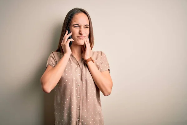歯の痛みや歯の病気のために痛みを伴う表現で手で口に触れる白い背景の上にスマートフォンで会話をしている若い美しい女性 歯医者の概念 — ストック写真