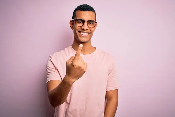 ピンクの背景にカジュアルなTシャツと眼鏡を身に着けているハンサムなアフリカ系アメリカ人男性ベッコーニングはここに来て手でジェスチャー歓迎幸せと笑顔 — ストック写真