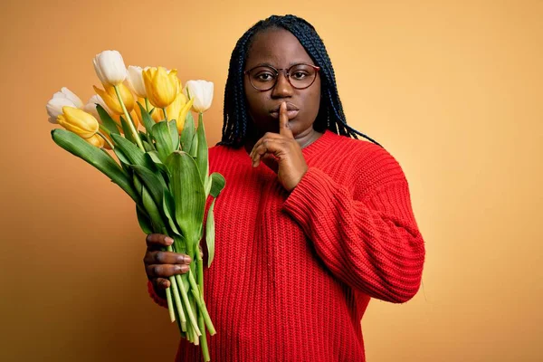 年轻的非洲裔美国人 加上头戴辫子拿着一束黄色郁金香花的女人 请求安静 手指放在嘴唇上 沉默和秘密概念 — 图库照片