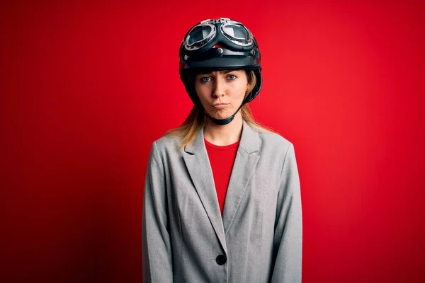 若い美しいブロンドのオートバイの女性は 赤い背景の上にオートバイのヘルメットをかぶって落ち込んでおり 苦痛のために心配し 怒って恐れて泣いています 悲しい表情 — ストック写真