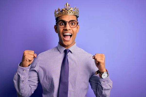 年轻英俊的非洲裔美国人 头戴金冠 头戴紫色背景的王冠 高举双臂 睁开眼睛 为成功感到惊奇和惊奇 赢的概念 — 图库照片