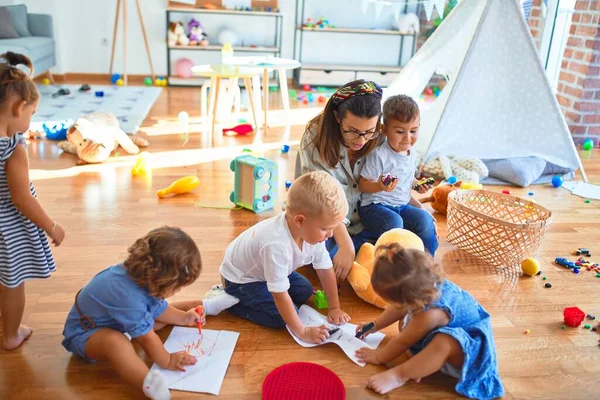 幼儿园里 漂亮的老师和一群小孩坐在地板上 用纸笔画着许多玩具 — 图库照片