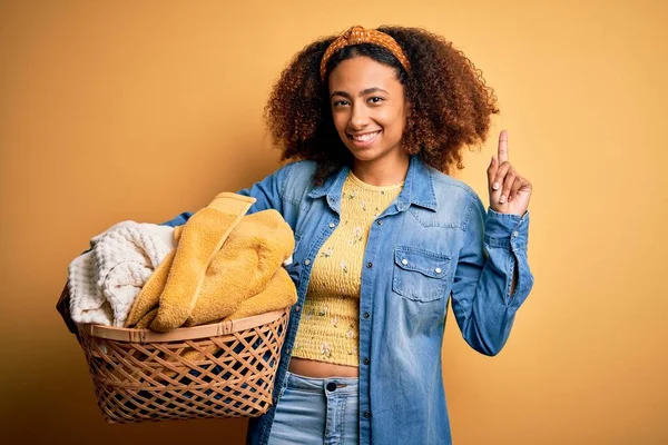 若いですアフリカ系アメリカ人女性とともにアフロヘア保持ウィッカーバスケットで服とともに驚きでアイデアや質問を指差す指で幸せな顔 ナンバーワン — ストック写真