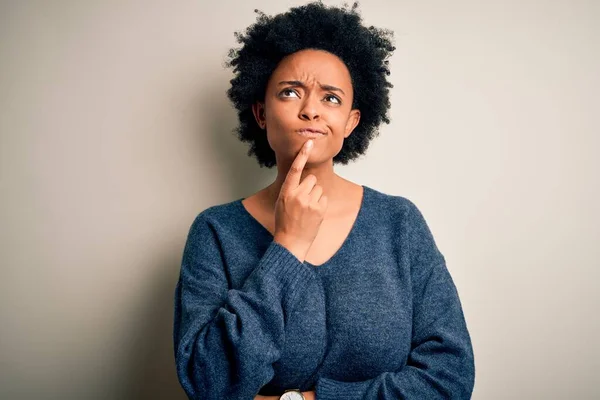 Young beautiful African American afro woman with curly hair wearing casual sweater Thinking concentrated about doubt with finger on chin and looking up wondering