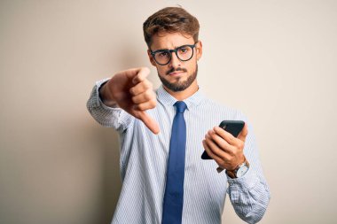 Genç işadamının beyaz arka planda akıllı telefon kullanması kızgın bir yüz, olumsuz işaret baş parmakları aşağıda, reddedilme konsepti.