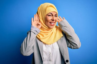 Orta yaşlı esmer iş kadını, mavi arka planda geleneksel Müslüman tesettüre bürünmüş iki elini de kulak hareketlerinde, dedikoduya meraklı olarak duymaya çalışıyor. İşitme problemi, sağır