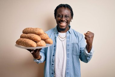 Genç Afrikalı Amerikalı adam elinde sağlıklı ekmeği beyaz arka planda tutarak gururla bağırıyor ve zaferi ve başarıyı kutluyor. Çok heyecanlı, coşkulu bir duygu.