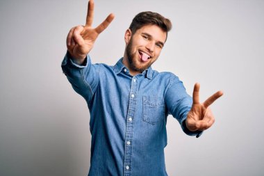 Sakallı, mavi gözlü, sıradan bir kot gömlek giyen, dili dışarı fırlamış ve parmaklarını zafer işareti yapan genç, sarışın bir adam. İki numara..