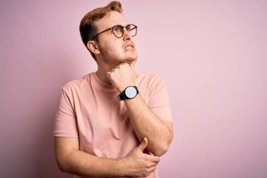 Genç, yakışıklı, günlük tişört giyen, pembe arka planda duran bir adam bir soru hakkında endişeli ve gergin bir şekilde düşünüyor.