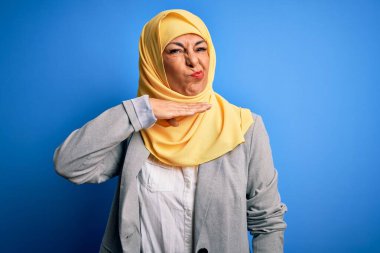 Orta yaşlı esmer iş kadını. Mavi arka plan üzerine geleneksel başörtüsü takmış. Bıçak gibi elleriyle boğazını kesiyor.