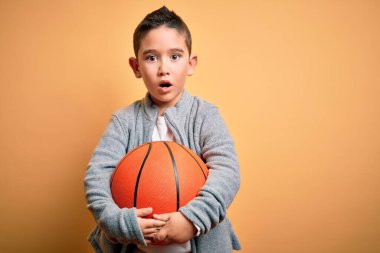 Küçük çocuk basketbol topuyla oynuyor. Sarı arka planda. Şaşırmış bir yüzle korkmuş ve korku ifadesinden heyecanlanmış.
