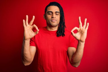 Genç, Afro-Amerikan Afrikalı, rastalı kırmızı tişört giyen rahat ve gözleri kapalı gülümseyen parmaklarıyla meditasyon hareketi yapan yakışıklı bir adam. Yoga konsepti.