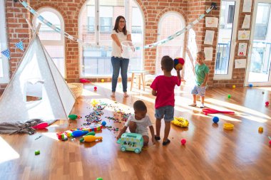 Anaokulunda bir sürü oyuncağın etrafında basketbol oynayan genç ve güzel öğretmenler ve yeni yürümeye başlayan çocuklar.