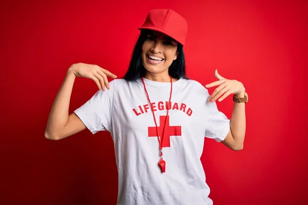 若い美しいヒスパニック系のライフガードの女性は 保護Tシャツを着て 顔に笑顔で自信を持って見て笛 誇りと幸せ指で自分自身を指して — ストック写真