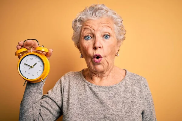 Sarı Arka Plan Üzerinde Alarm Saati Tutan Yaşlı Güzel Bir — Stok fotoğraf