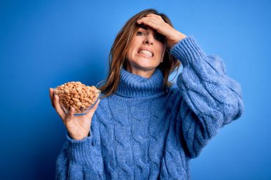 Mavi arka planda fıstık ezmesi olan genç ve güzel esmer kadın elleri başının üstünde, utanç ve şaşkınlık dolu, sinirli ve hayal kırıklığına uğramış bir halde. Hata için korku ve üzüntü.