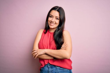 Genç esmer kadın pembe izole edilmiş arka plan üzerine gündelik bir tişört giyip kollarını kavuşturup kameraya bakarak gülümsüyor. Pozitif kişi.