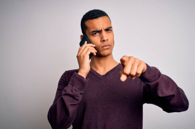 Genç ve yakışıklı Afro-Amerikalı adam akıllı telefondan konuşuyor kamerayı işaret ediyor ve sen, el işareti, ön taraftan pozitif ve kendinden emin bir jest.