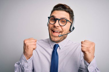 Genç çağrı merkezi operatörü mavi gözlü, gözlüklü ve kulaklıklı adam kolları açık ve gözleri açık bir şekilde başarıyı kutluyor ve şaşırıyor. Kazanan konsept.