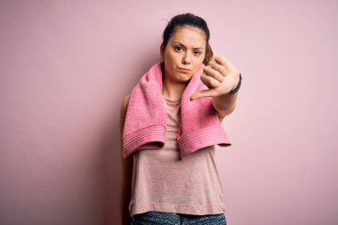 Genç ve güzel esmer bayan spor giyiniyor ve pembe arka plan üzerinde havlu var mutsuz ve kızgın görünüyor reddedilmiş ve olumsuz. Kötü ifade.