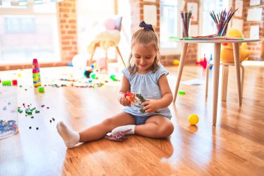 Genç, güzel sarışın kız anaokulunda oyuncaklarla oyun oynuyor, gülümseyerek evde dinozor oyuncaklarıyla oynuyor.