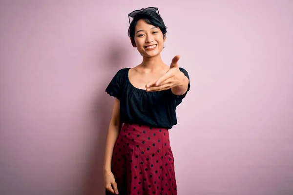 年轻美丽的亚洲女孩穿着休闲装 站在孤立的粉色背景上 开心地微笑着 伸出援助和接纳的手 — 图库照片