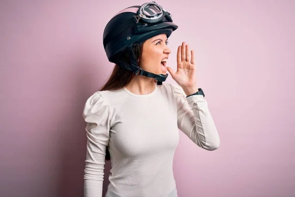 年轻美丽的骑摩托车的女人 蓝眼睛 戴着红色的头盔 背对着粉红的背景大喊大叫 双手放在嘴边大声尖叫 传播概念 — 图库照片