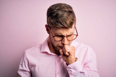 Sakallı, mavi gözlü, pembe tişörtlü, gözlüklü, kendini iyi hissetmeyen ve soğuk algınlığı veya bronşitin belirtisi olarak öksüren sarışın genç bir adam. Sağlık hizmeti kavramı.