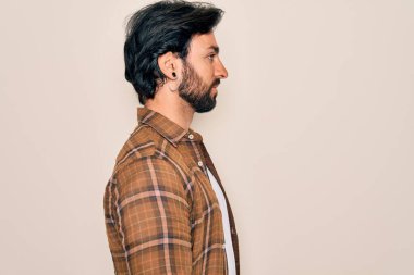 Genç, yakışıklı, bohem, hippi tarzı giyinmiş bir adam izole bir arka planda duruyor. Yan yana bakıyor, rahat bir görünüm sergiliyor, kendine güvenen bir gülümsemeyle doğal bir poz veriyor..