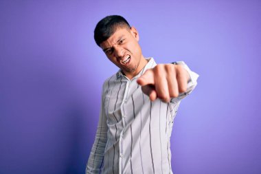 Zarif iş gömleği giyen genç yakışıklı İspanyol adam mor arka planda dikiliyor. Kameraya kızgın ve sinirli olduğunu gösteriyor.