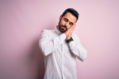 Sakallı genç yakışıklı bir adam pembe arka planda dikiliyor uykusuzca uyuyor, hayal kuruyor ve elleriyle poz veriyor, gözleri kapalı gülümsüyor..