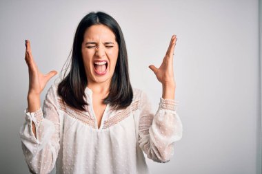 Mavi gözlü genç esmer kadın izole edilmiş beyaz arka plan üzerine gündelik tişört giyerek başarının çılgınlığını kollarını kaldırarak ve gözlerini kapayarak heyecanla bağırarak kutluyor. Kazanan konsept