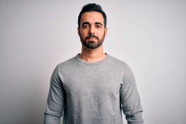 Sakallı, beyaz arka planda sıradan bir süveter giyen yakışıklı genç bir adam. Yüzünde ciddi bir ifadeyle rahatlamış. Basit ve doğal bir şekilde kameraya bakıyorsun..