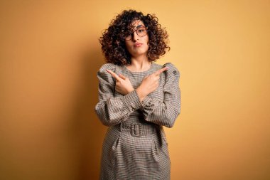 Güzel bir Arap iş kadını. Elbise ve gözlük takıyor. Sarı arka planda duruyor.