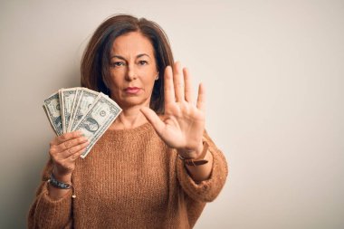Orta yaşlı esmer kadın, elinde bir dolar banknotla izole edilmiş arka planda, dur işareti ve ciddi ve kendinden emin bir ifadeyle savunma jesti yapıyor.