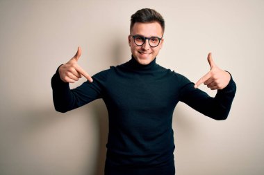 Gözlüklü, gözlüklü, rahat bir süveter giyen, kendine güvenen, gülümseyen, kendini gururlu ve mutlu gösteren genç beyaz bir adam..