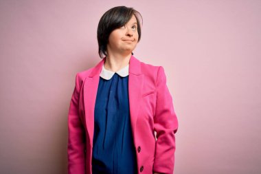 Genç Down sendromlu iş kadını pembe arka planda gülümseyip yan tarafa bakıyor ve düşünüyor..