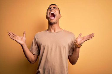 Sarı arka plan üzerinde sıradan tişörtler giyen genç ve yakışıklı Afro-Amerikan erkeği kollarını kaldırmış ve gözlerini kapatmış heyecanla haykırarak başarıyı kutluyor. Kazanan konsept