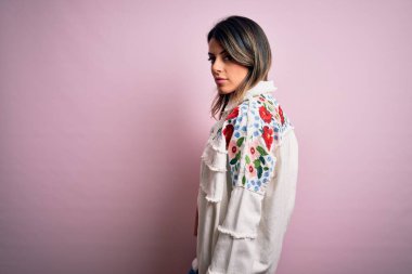 Moda kıyafetleri giyen genç ve güzel bir kadın. Manken, sokak tarzı giyiniyor. Pembe arka planda dikiliyor.