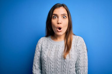 Güzel, genç bir kadın mavi yünlü bir arka plan üzerinde dikilmiş korku, korku ve heyecan dolu bir yüz ifadesiyle şok olmuş ve korkmuştu..