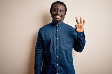 Beyaz arka plan üzerinde duran ve gülümseyen, kendinden emin ve mutlu gülümseyen genç, Afro-Amerikalı bir adam..