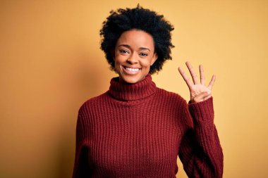 Kıvırcık saçlı, balıkçı yaka kazak giyen, dört numaralı parmaklarıyla işaret eden, kendine güvenen ve mutlu gülümseyen güzel Afro-Amerikan kadın..