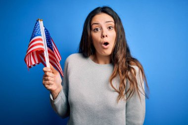 Genç, güzel, vatansever kadın elinde Amerikan bayrağı tutarak 4 Temmuz 'u kutluyor. Şaşırmış bir ifadeyle korkmuş ve heyecanlanmış bir şekilde.
